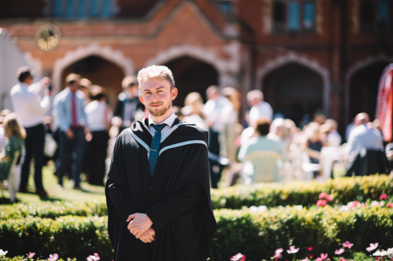 male student standing in the grounds of Queen's University in graduation gown