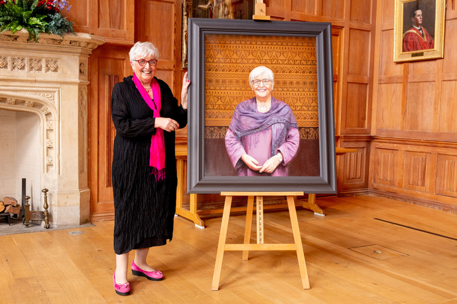 Professor Carol McGuinness standing beside her portrait in Queens Great Hall