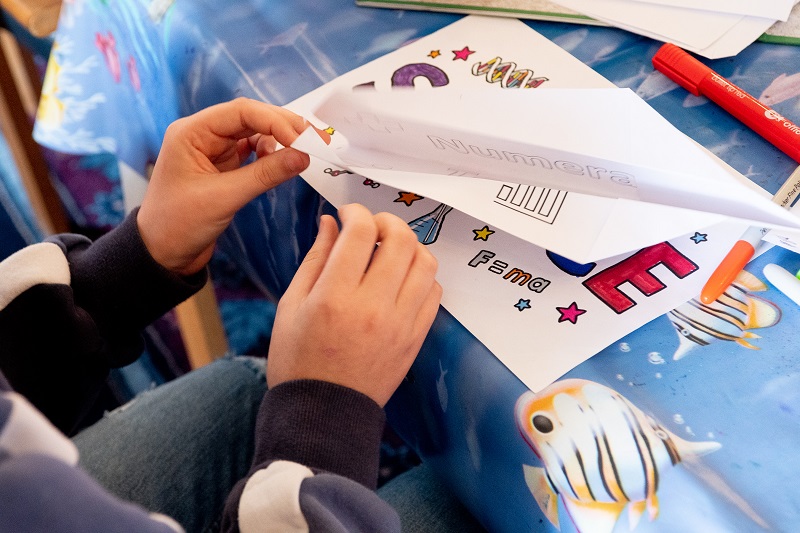 child making paper aeroplane from colouring book page