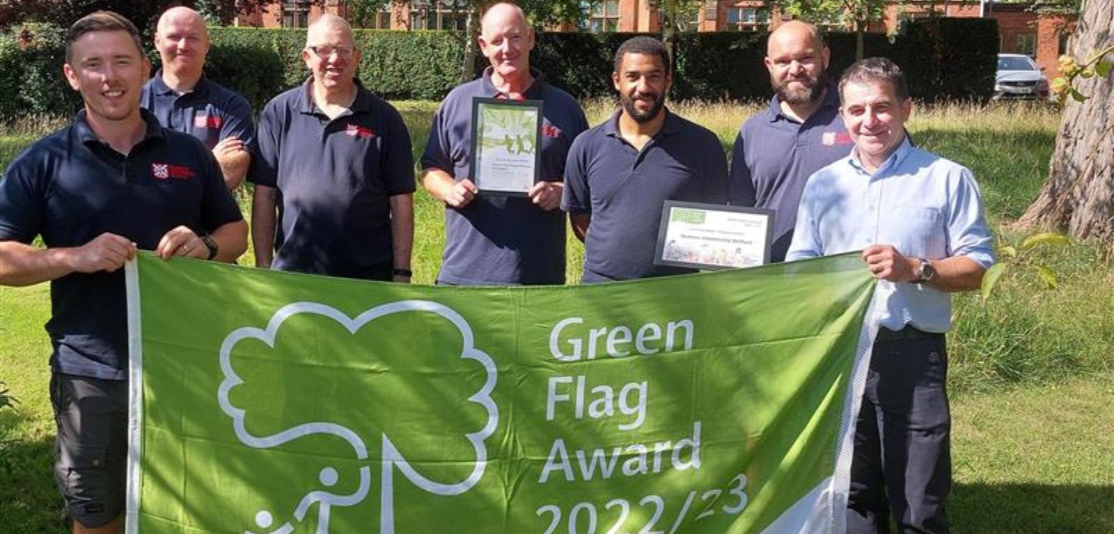 The Garden and Grounds team standing on a lawn holding a Green Flag Awards banner