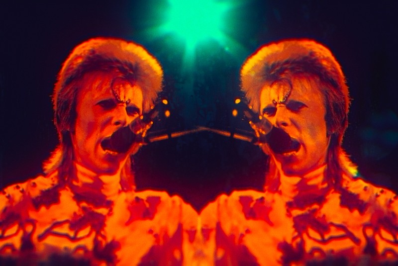 Still from film Moonage Daydream showing a mirror image of David Bowie in concert singing into a microphone