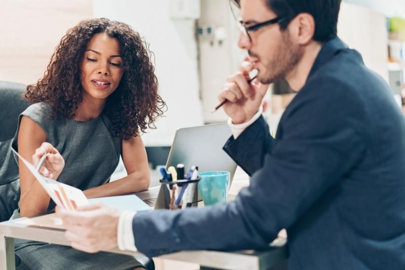 female leader pointing to graphic on sheet of paper being held by male colleague