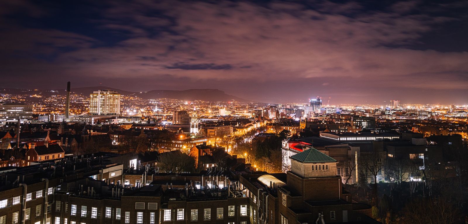 A dramatic view of the Belfast Skyline at night, light up by the lights of buildings and street lighting, from above Queen's University Belfast's David Keir building