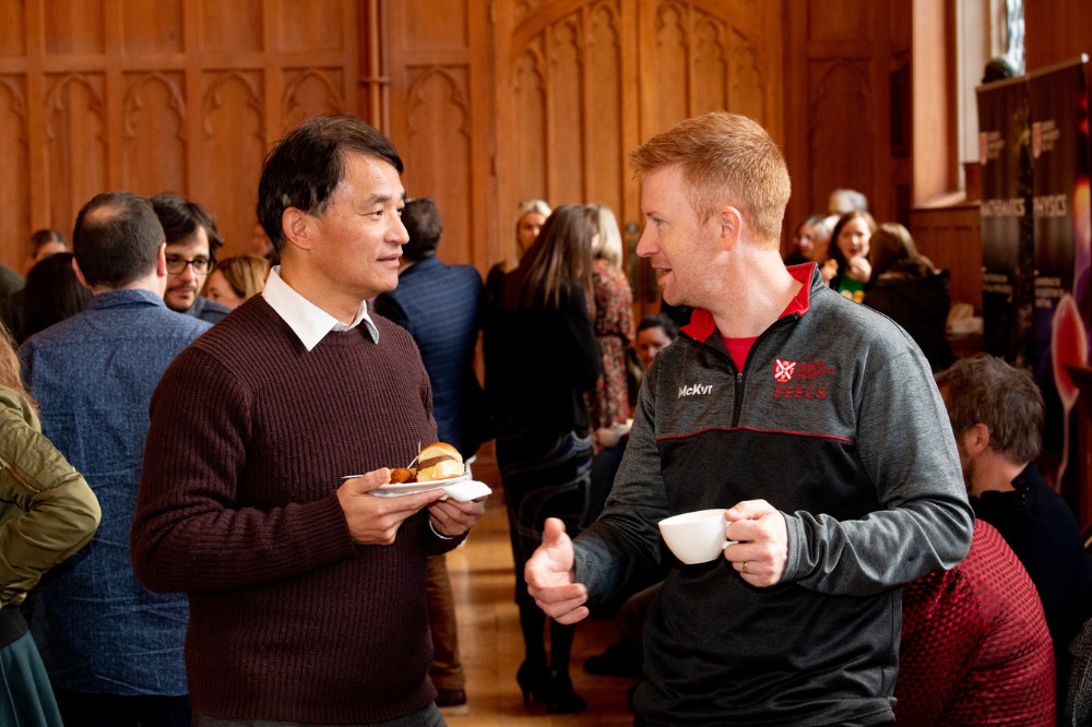 two men chatting over celebratory buffet lunch in a busy Great Hall at Queen's University Belfast