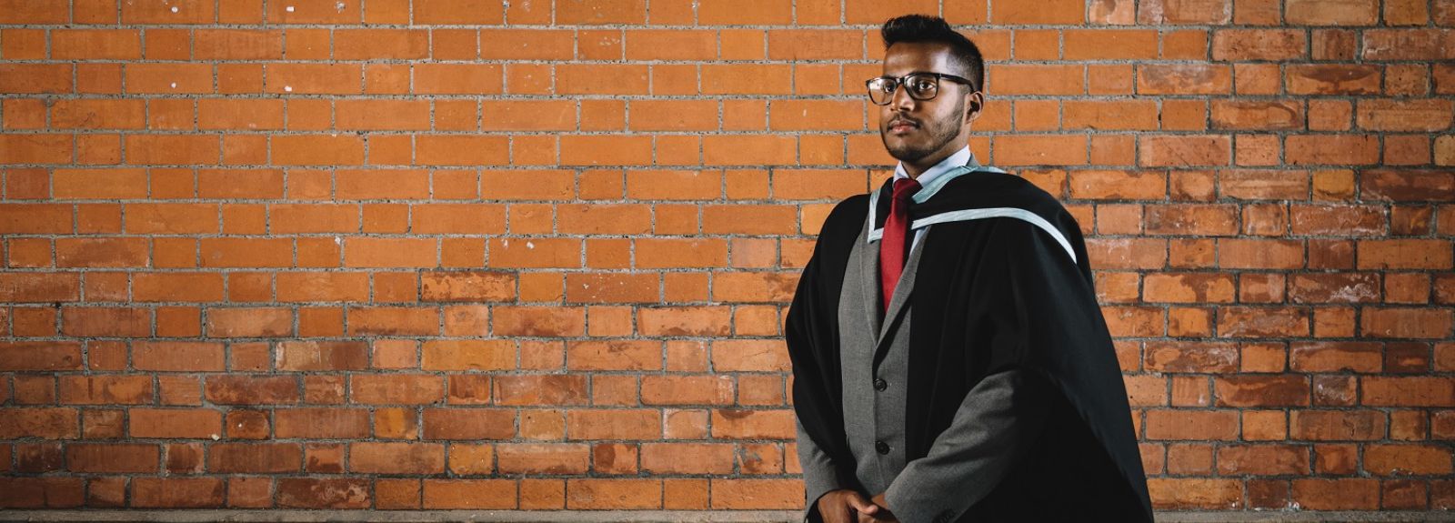 male student standing in a room getting a graduation photo taken in graduation gown