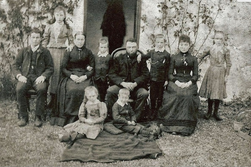 black and white photo of a pre-1925 family sitting/standing outside a cottage