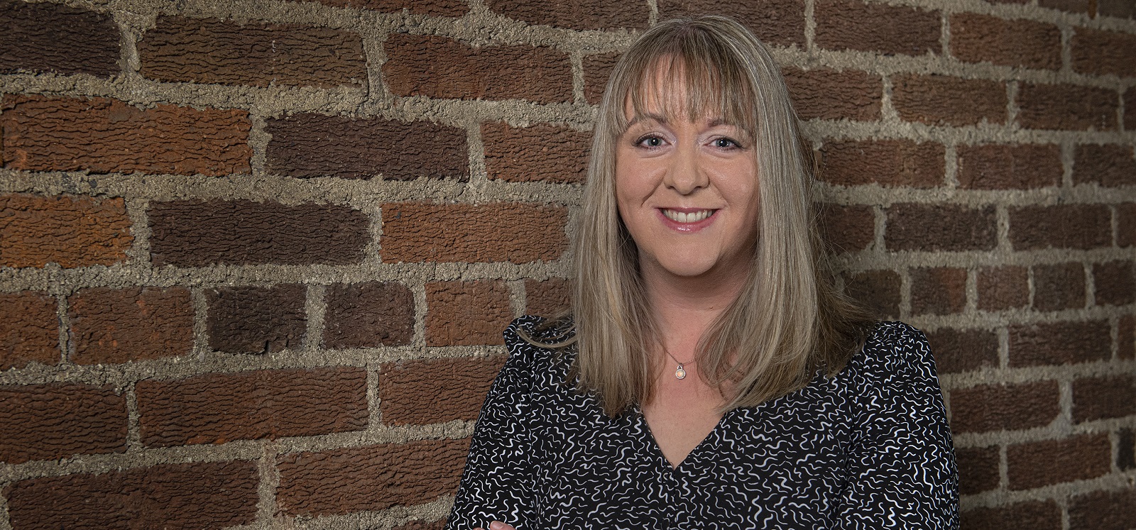 Dr Gemma Catney standing against a red brick wall