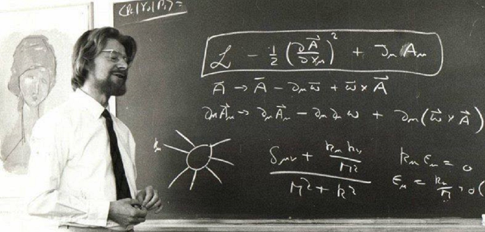 John Stewart Bell standing in front of a blackboard on which equations are written