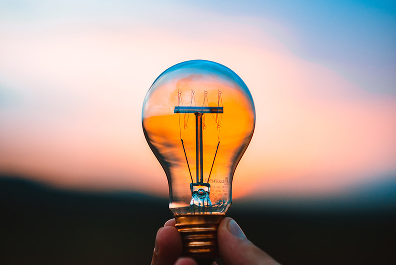 A hand holding a lightbulb against a sunset sky