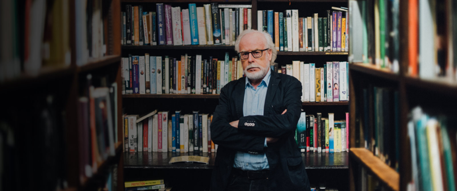 John Wilson Foster profile picture.  John is pictured in a library, surrounded by books on shelves.