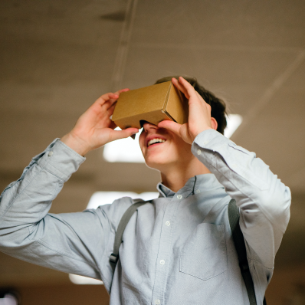 A teenager is holding a VR headset made of cardboard