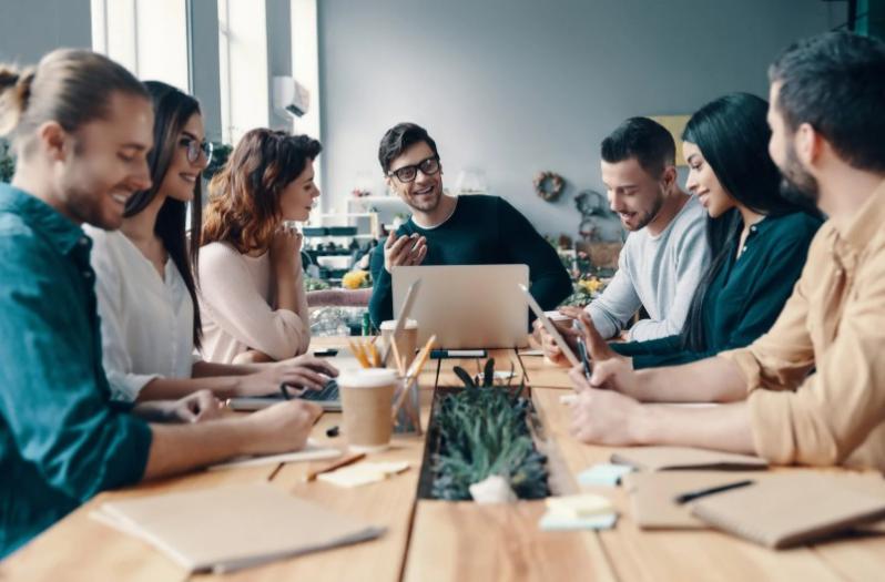 A group of corporate professionals sitting around a table actively engaged on a laptop and in discussion with one another