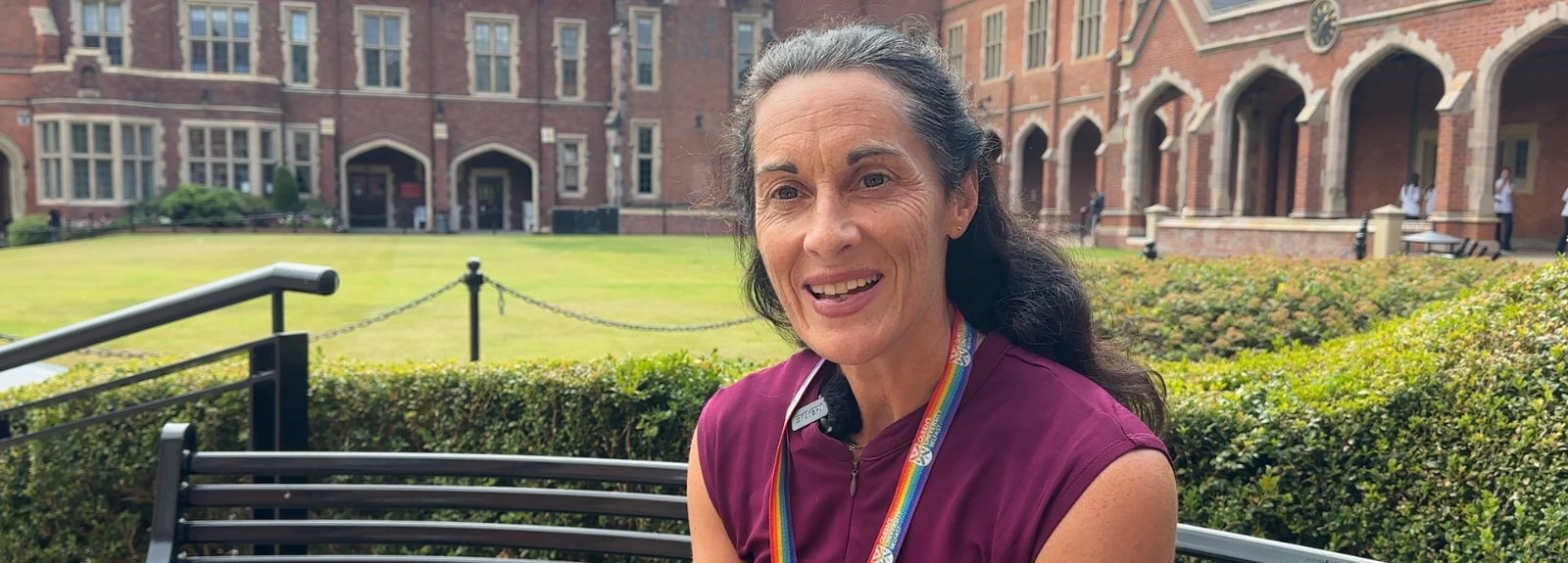 Dark haired lady sitting on a black bench in the quad of QUB with a grassy area as a backdrop
