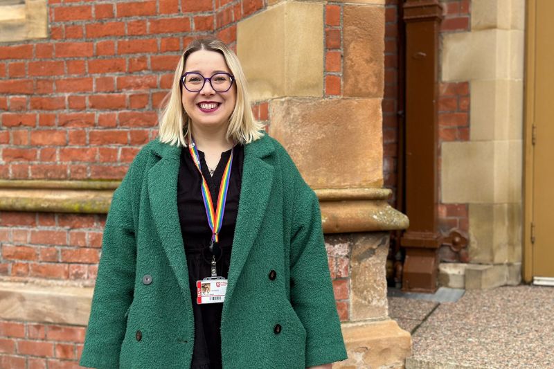 woman wearing glasses smiling to camera outside a red-brick building