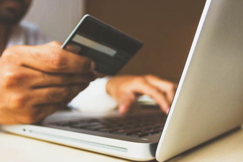 A person holds a bank card whilst looking at a laptop