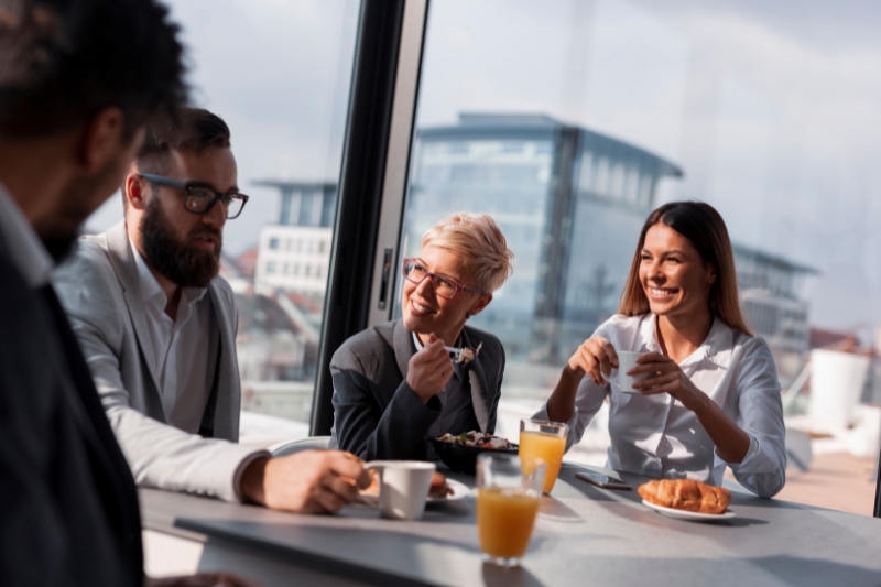 two men and two women in business dress meeting over a light breakfast in a bright indoor space