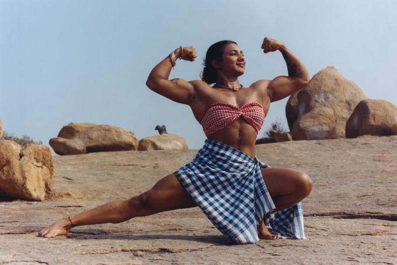 female bodybuilder of South Asian origin striking a pose in a dry, rocky area