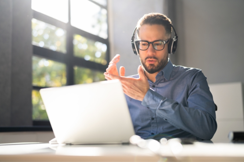 man wearing glasses in clean, bright office space engaged in online training or meeting