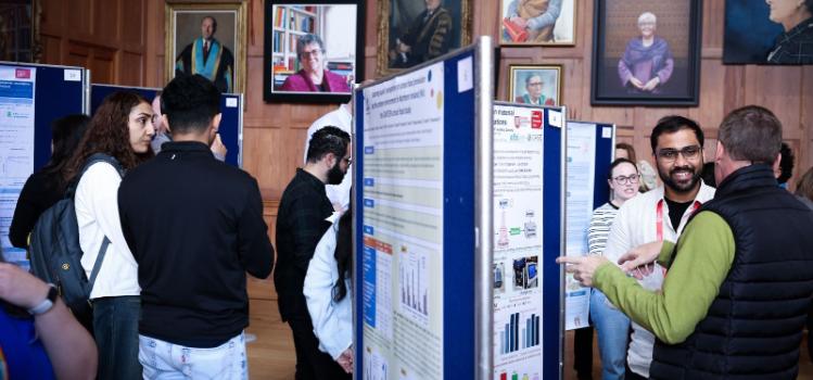 people standing and conversing at a research poster exhibition in an old wood-paneled hall with portraits hanging in the background