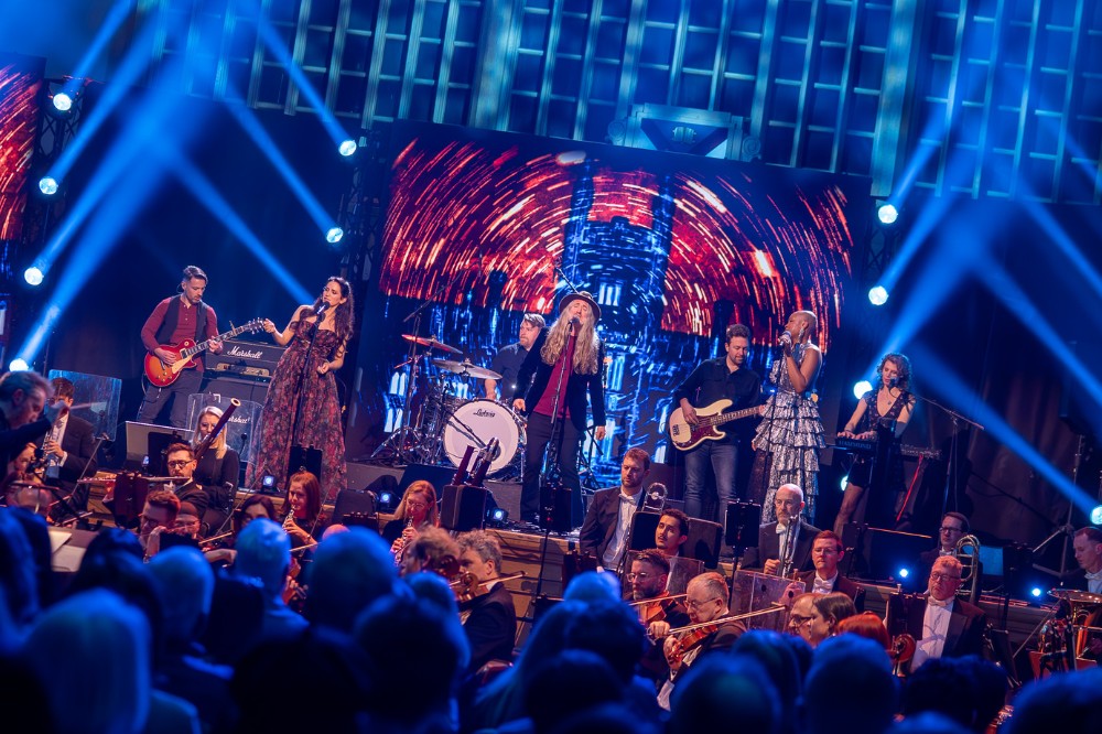a band performing on stage in the background with seated audience pictured from behind in the foreground