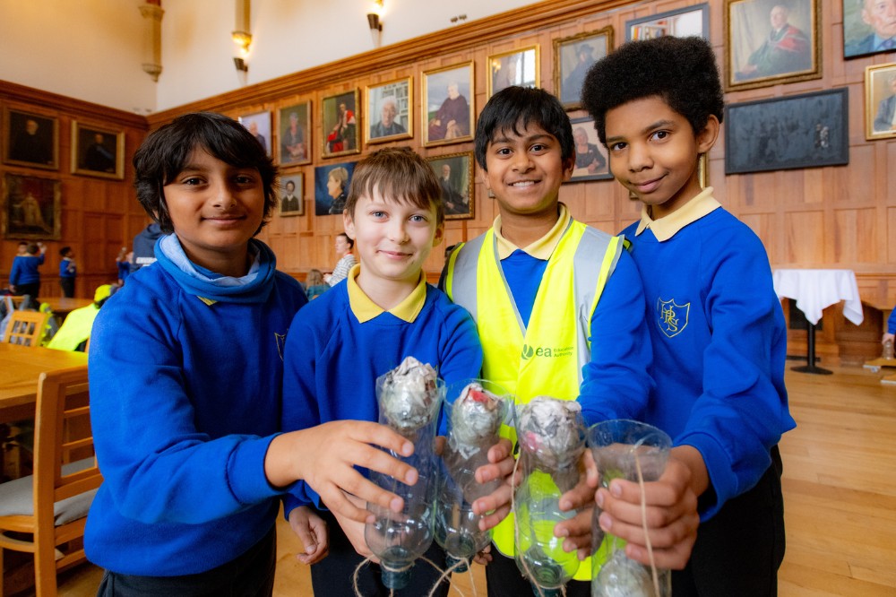 four school children holding craft handmade from recyclable materials at one of the events in Queen's arts and sustainability festival Reach '24 in the Great Hall