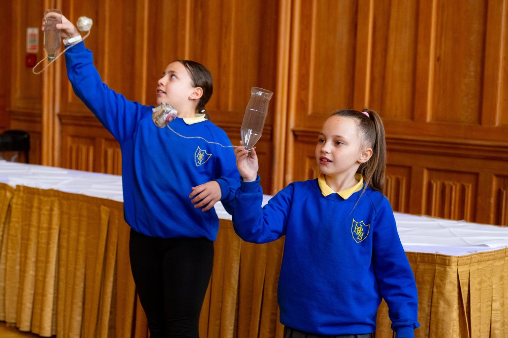 two school children holding a game handmade from recyclable materials at one of the events in Queen's arts and sustainability festival Reach '24 in the Great Hall