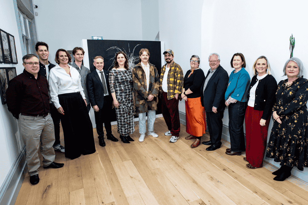 group of smiling people standing side by side posing for the camera in an art gallery