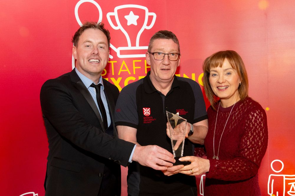man being presented with a trophy by a man and woman at an indoor event