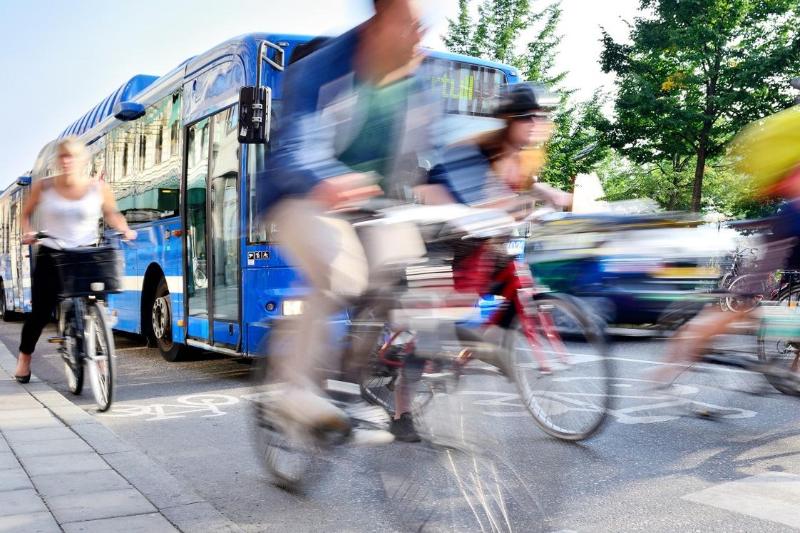 blurry, fast-moving people cycling on a busy road with buses and cars on a bright day