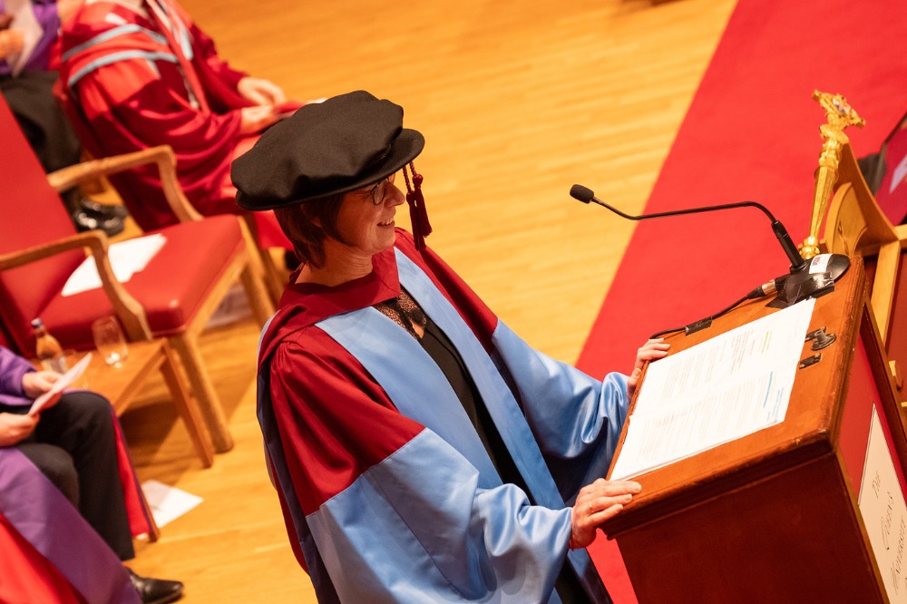 aerial view of an academic in graduation robe and hat addressing an audience in a large hall