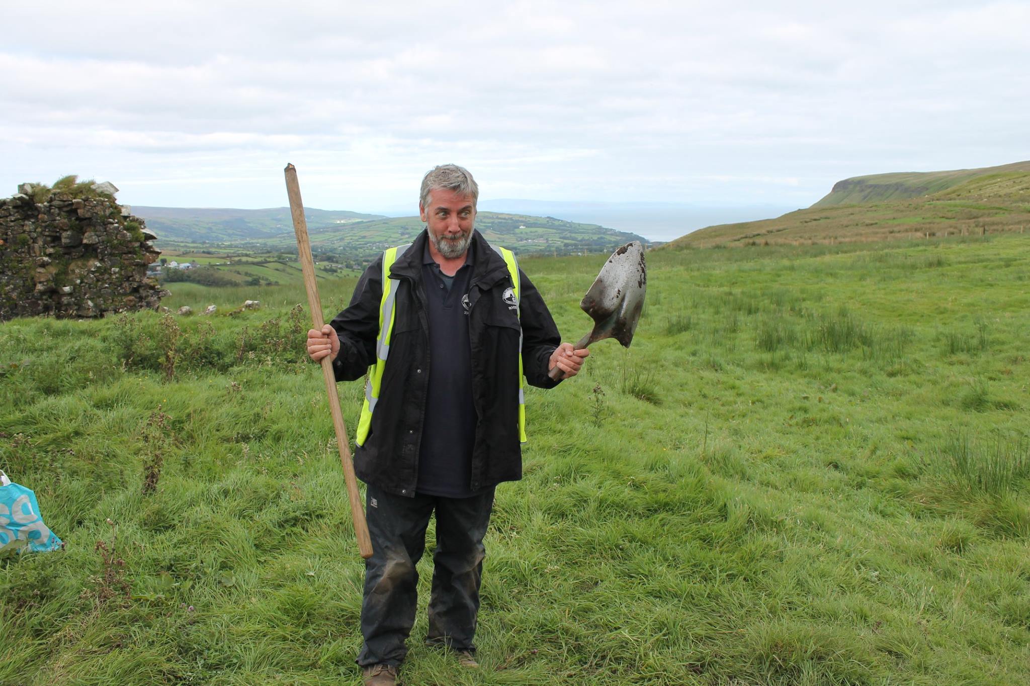 Ruairí Ó Baoill standing in a field holding a broken shovel